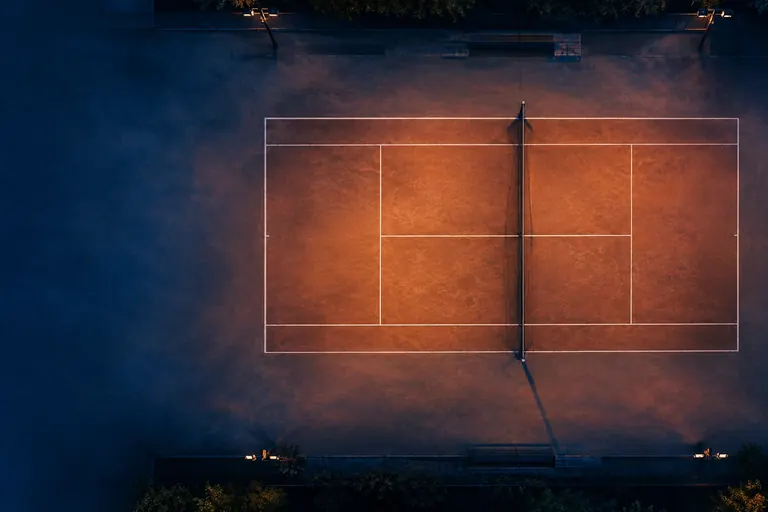 An empty tennis court seen from above, a visual anchor for a page comparing tennis odds across venue types.
